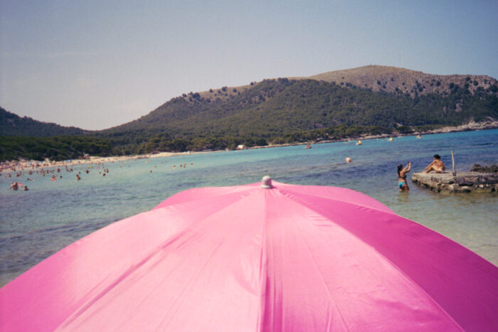 Beach scene with a pink umbrella and coastal view.