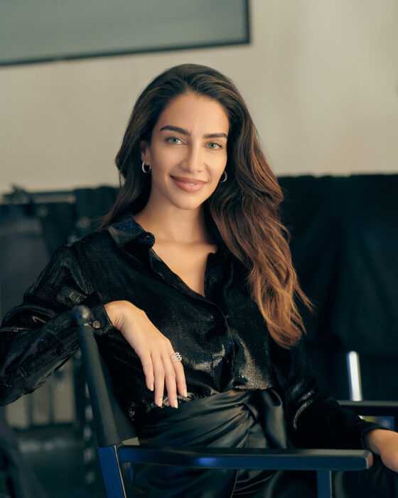 Lifestyle portrait of woman in black satin shirt seated on a chair.