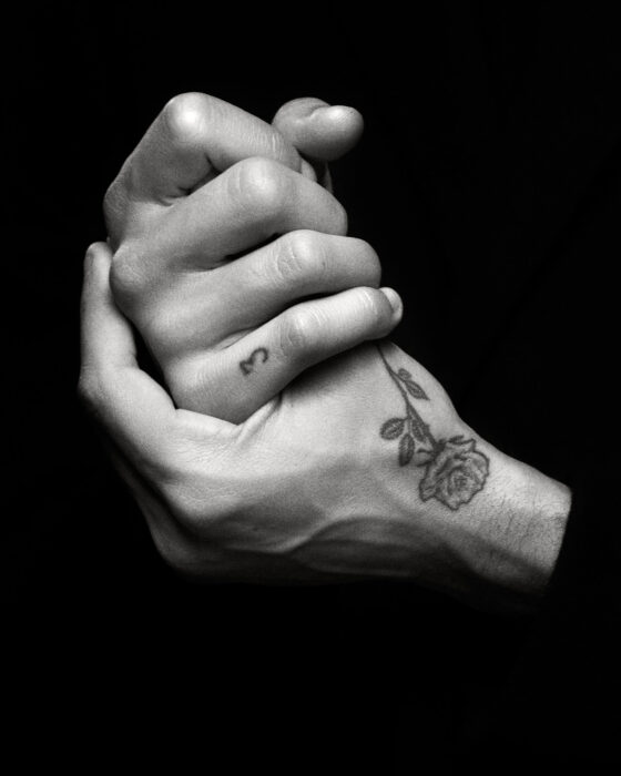 Black-and-white close-up of clasped hands showing tattoos.