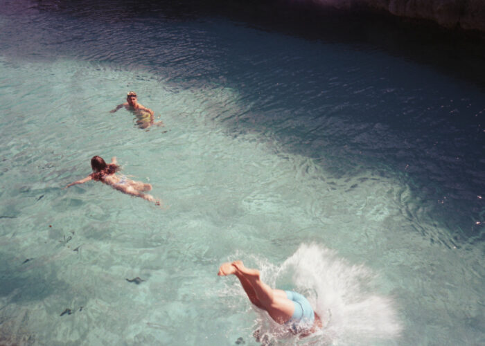 Aerial travel photograph of people swimming and diving in turquoise sea water.
