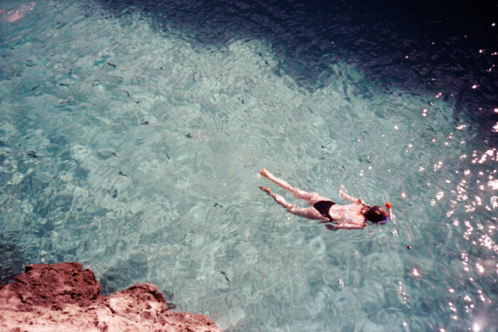 Aerial travel photograph of a person swimming in clear turquoise water.