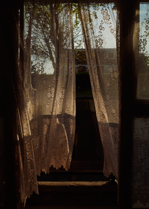 Documentary image of lace curtains hanging in a doorway, moody light.