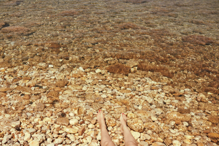 Close-up travel image of a pebbled beach and bare feet.