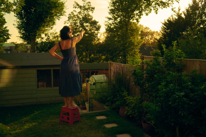 Lifestyle image of a woman standing in a garden in evening light.
