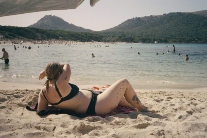 Lifestyle photograph of a woman lying on a sandy beach.