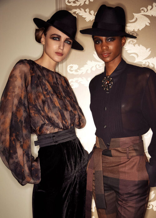 Editorial fashion portrait of two women in hats and patterned outfits.