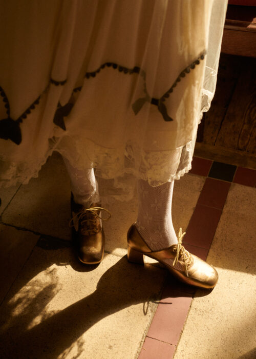 Fashion detail image of woman's legs and shoes in an embroidered dress.