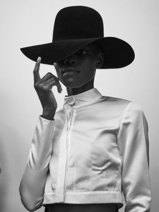 Black-and-white fashion portrait of woman in wide-brim hat and satin jacket.