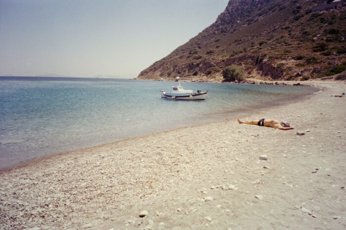 Coastal landscape with a boat and a person lying on the beach.