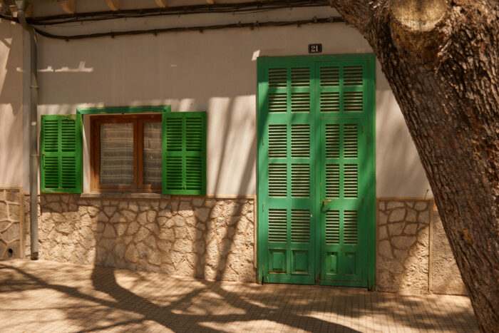 Documentary image of a house with green shutters beside a tree.