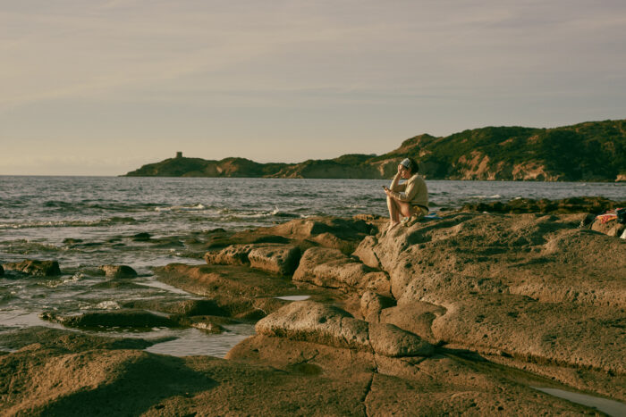 Coastal landscape with a person seating on rocks by the sea.