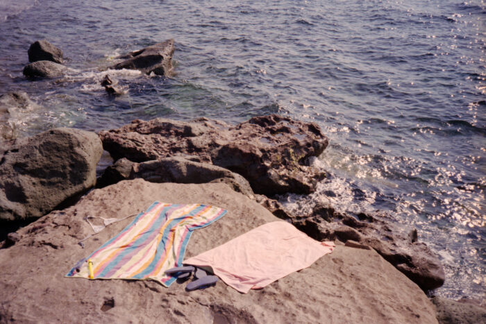 Lifestyle image of a striped towel and clothing laid on coastal rocks.