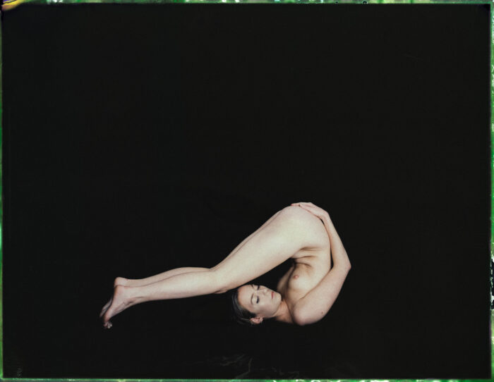 Nude portrait in polaroid style, woman reclining against a dark backdrop.
