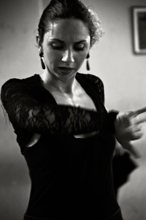 Studio portrait of woman in black lace top with hands raised in flamenco gesture.