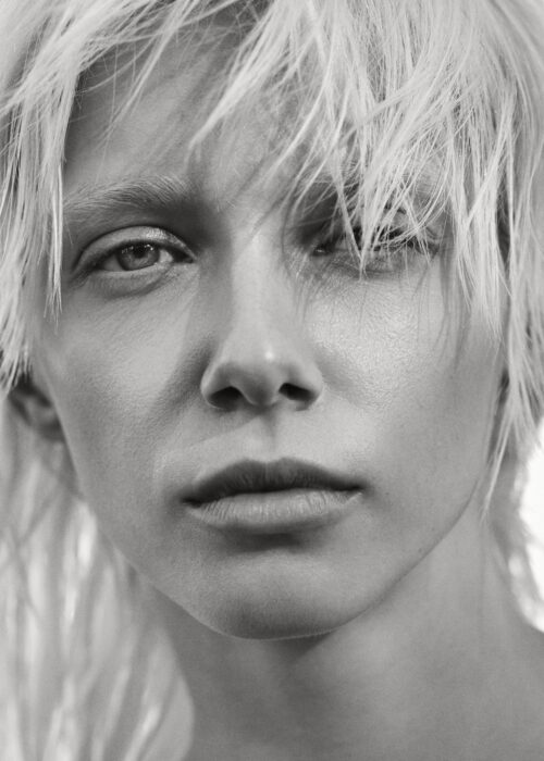 Black-and-white beauty portrait of woman with tousled blonde hair, close crop.