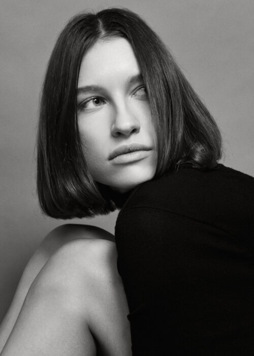Black-and-white portrait of woman with dark bob looking over her bare shoulder.