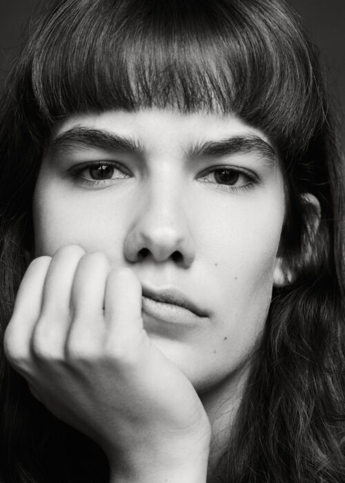 Black-and-white close-up portrait of woman resting chin on her hand.