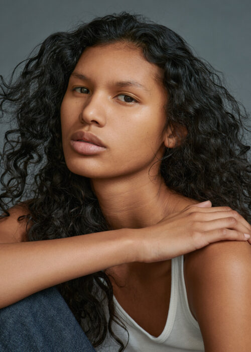 Close-up beauty portrait of woman with hand resting on her shoulder.