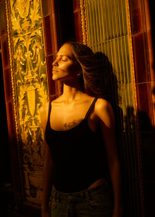 Fashion portrait of woman in black top lit warmly beside an ornate doorway.