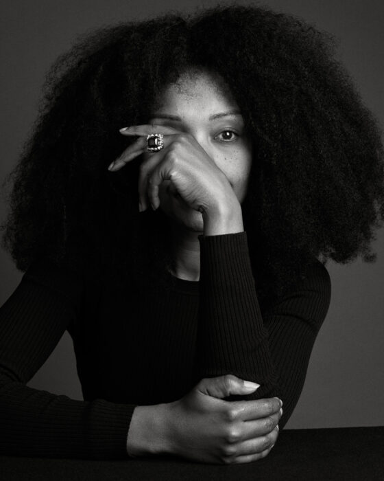 Black-and-white portrait of woman with curly hair, hand resting near her face.
