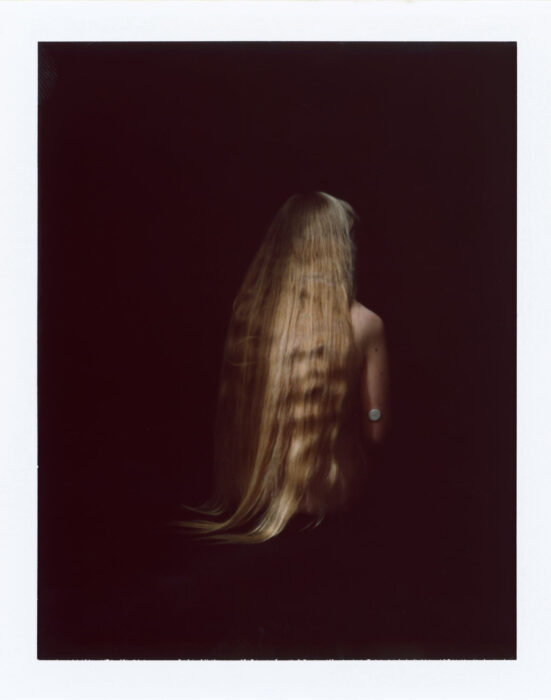 Polaroid-style portrait of long hair seen from behind, dark red backdrop.
