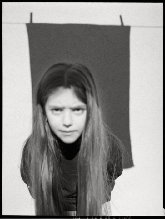 Black-and-white portrait of girl with long hair against a fabric shadow.