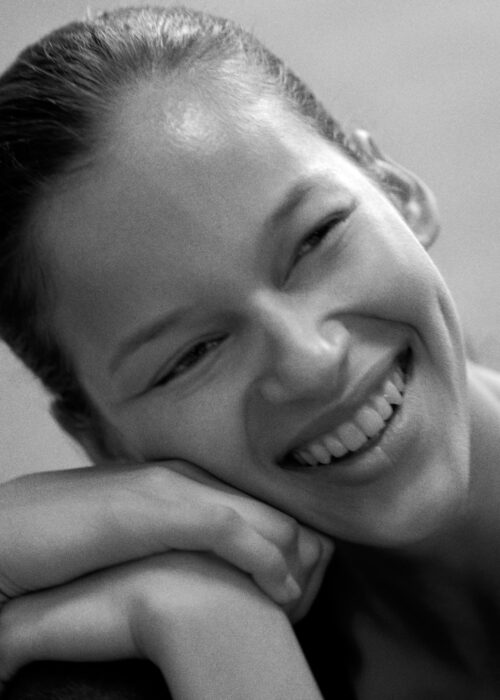 Black-and-white beauty portrait of smiling woman resting her chin on her hands.