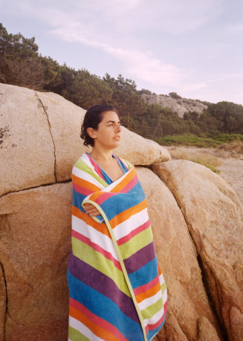 Travel portrait of a woman wrapped in a striped towel by rocks.
