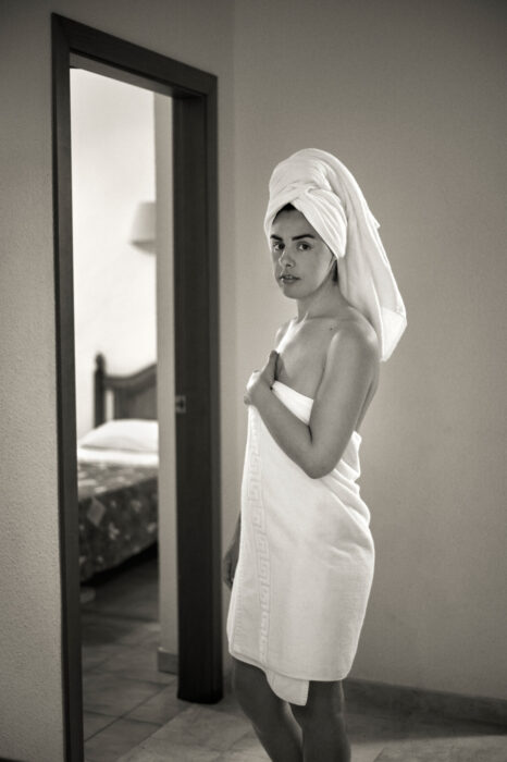 Black-and-white lifestyle portrait of woman wrapped in a towel in a hotel room.