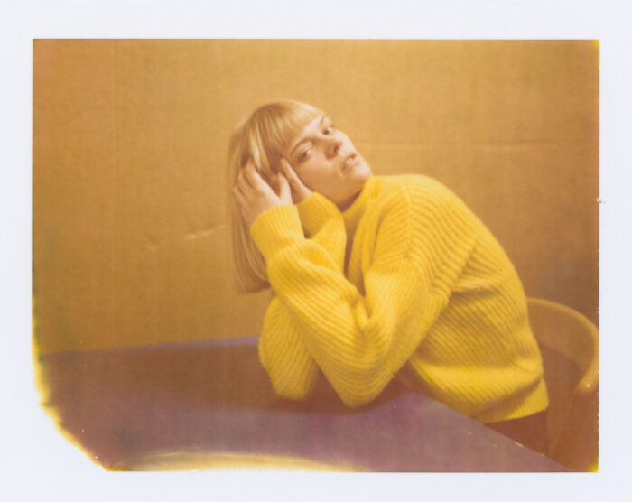 Polaroid-style portrait of woman in yellow sweater leaning back